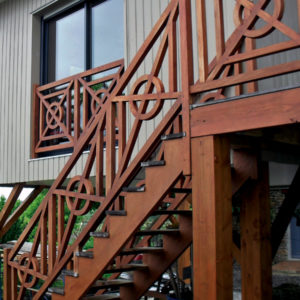 Escalier extérieur droit en bois sans contremarches d'une maison sur en bois sur pilotis. Double crémaillère avec marches sans contremarches. Rampe et garde corps seuil porte et fenêtres en bois décoration celtique (croix), poteaux standards carrés.