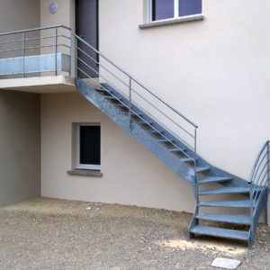 Escalier extérieur quart tournant bas en métal galvanisé. Marches perforées. Rampe : main courante et lisses cylindriques. Garde corps : main courante et lisses cylindriques droites et coudées, soubassement tôle perforée.