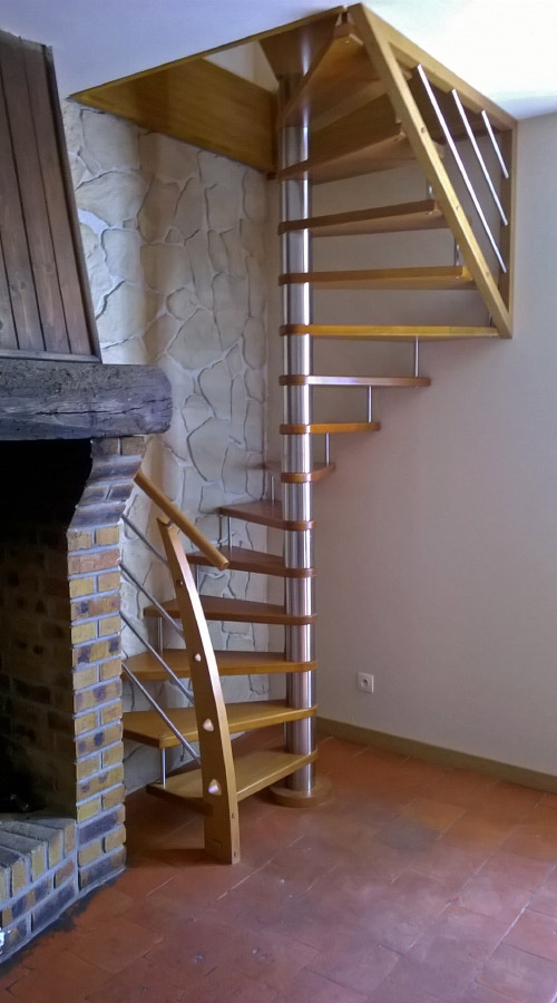 Escalier hélicoïdal (colimaçon) en bois et métal, sans contremarches. Noyau central avec entretoises en métal. Main courante, poteaux, marches et claustra en bois teinte chêne clair. Rampe et Claustra design : pitons et lisses en acier type tubes inox.