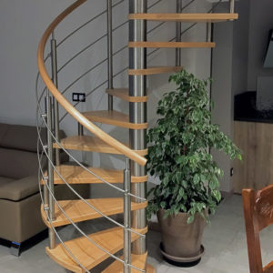 Escalier hélicoïdal (colimaçon) en bois (teinte chêne clair) et métal, sans contremarches. Noyau central en métal brillant, marches en bois. Main courante en bois rond. Poteaux et pitons et lisses métal en acier inox.