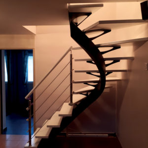 Escalier double quart tournant intermédiaire sans contremarches en bois et métal. Limon central courbé en bois teinte noire, ailes d'avion en métal teinte noire, marches en bois laquées blanches. Rampe : main courante en bois rond laqué blanc, poteaux, en métal couleur chrome, lisses câbles inox
